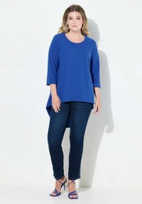 Top blu, a maniche lunghe con scollatura rotonda, abbinato a jeans blu scuro con dettagli a borchie lungo i lati.