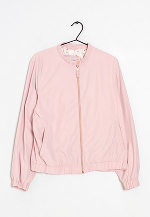 Chaqueta bomber rosa claro con cremallera frontal, cuello con botón a presión, puños elásticos y bajo elástico, colgada en una percha negra sobre fondo blanco.