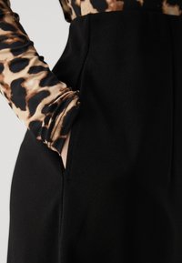 Black fabric trousers with a structured fit, featuring side pockets, paired with a long-sleeve top in a brown and black animal print.