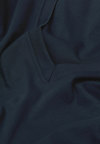 Niebieski materiał o gładkiej teksturze, lekko drapowany, z dekoltem w serek oraz subtelnymi przeszyciami, podkreślającymi jego miękką, elastyczną jakość.