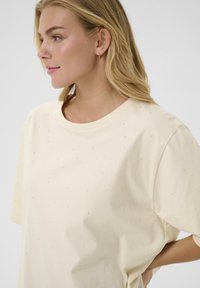 Cremfarvet t-shirt lavet af blødt stof, med spredte juvel-lignende udsmykninger på forsiden og en afslappet pasform.