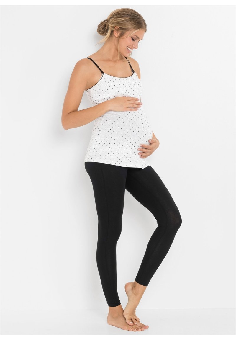 Top da maternità bianco a pois con spalline nere regolabili, abbinato a leggings neri. Tessuto morbido, linea aderente e design confortevole.