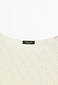 Zbliżenie na biały, teksturowany sweter z dzianiny z czarną metką Massimo Dutti wszytą wewnątrz kołnierza.