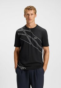 Sort t-shirt med kortærmer, der har et hvidt abstrakt linjemønster på tværs af brystet, lavet af et glat og let stof.