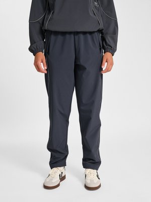 Osoba nosząca czarne spodnie sportowe z bocznymi szwami, czarną bluzkę z długim rękawem i białe trampki z czarnymi paskami.