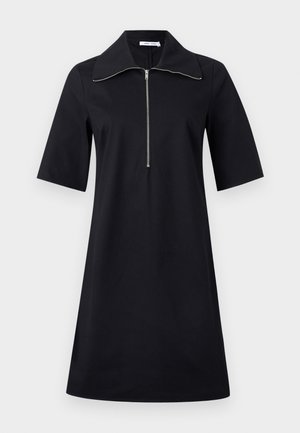 Svart knelengde kjole med korte ermer, vid krage og sølvfarget glidelås foran som går fra halsringningen til midten av brystet.