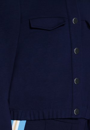 Veste courte bleu marine en tissu doux, avec boutons-pression, une poche avant et un ourlet froncé.