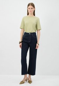 T-shirt verde a maniche corte con una vestibilità comoda, abbinato a jeans a gamba larga in denim scuro a vita alta. Eleganti scarpe basse verde oliva.