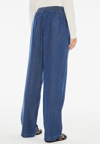 Pantaloni a gamba ampia in denim blu scuro, con vita elasticizzata e texture liscia. Il tessuto è leggero e leggermente fluido.