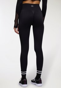 Leggings neri con vita alta, texture liscia e design aderente. Abbinati a scarpe nere con accenti bianchi e viola.