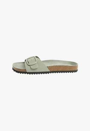 Slip-on sandal med lys grøn ruskindsrem, stor spænde, kork-fodtøj og sort rillede sål.