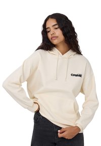 Kremowa bluza z kapturem, z kieszenią kangurzą, regulowanym sznurkiem na kapturze i czarnym napisem "CRIME" po lewej stronie klatki piersiowej. Materiał z mieszanki bawełny.