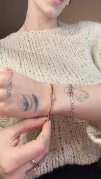 Auksu tonuota apyrankė su apskritu skaidriu akmeniu, turinti siaurą, lankstų dizainą. Dėvima ant tatuiruotos rankos, derinama su sidabro grandinėlių apyrankėmis.