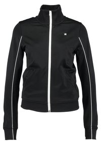 Chaqueta negra con cremallera y cuello alto, hecha de un tejido suave. Ribete blanco a lo largo de los hombros y por las mangas. Dos bolsillos laterales.