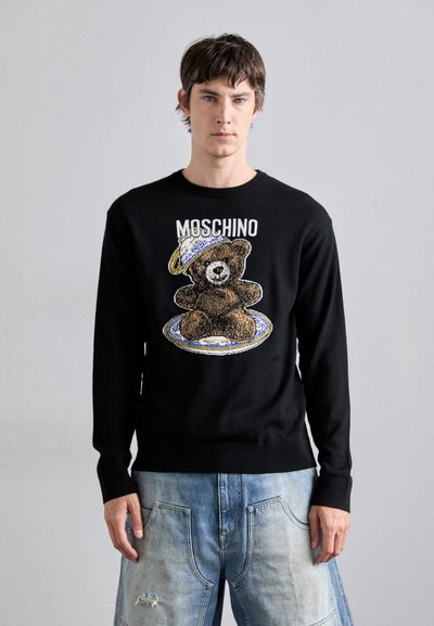 Zwarte gebreide trui met een berenafbeelding en een petontwerp op een bord, met "MOSCHINO" erboven in het wit gedrukt. De textuur is soepel en aansluitend.