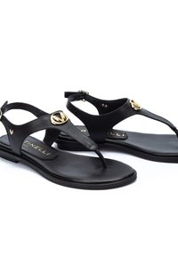 Sandales en cuir noir avec une semelle plate, design en tongs et accents circulaires dorés sur les brides. Boucle réglable à la cheville pour un ajustement parfait.