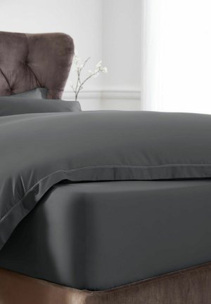 Graues Spannbettlaken und Kissenbezug auf einem Bett mit einem braunen gepolsterten Kopfteil und einer weißen Blume im Hintergrund.