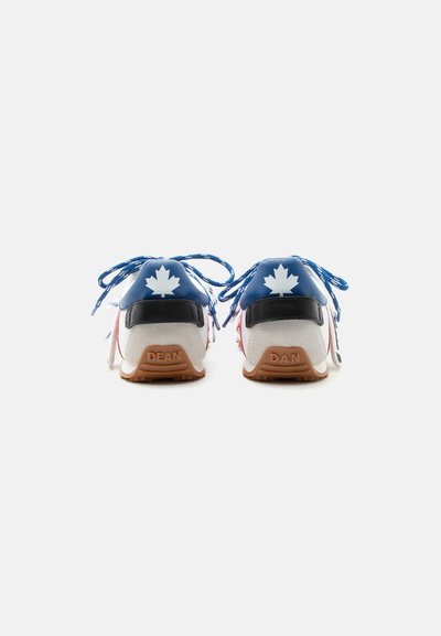 Paire de baskets blanches avec des lacets bleus, des languettes de talon bleues avec des logos de feuille d’érable blanche, et des semelles marron portant les inscriptions "DEAN" et "DAN".
