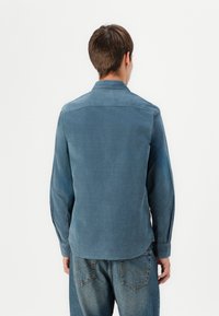 Dark blue long-sleeve shirt made of soft fabric, featuring a button-down collar, straight hem, and two-button cuffs. Worn over denim jeans.