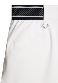 Białe spodnie z czarnym i białym paskiem elastycznym w poziome paski, z metalowym detalem w kolorze srebrnym i tylną kieszenią. Gładka faktura tkaniny.