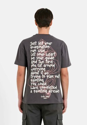 Grijze t-shirt met korte mouwen, voorzien van artistieke tekst en een eenvoudige lijntekening op de achterkant. De stof ziet er zacht en casual uit.