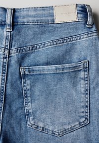 Svetle modré džínové kalhoty s zadní kapsou, viditelným švem a koženou etiketou na pase s nápisem "STREET ONE STUDIO."