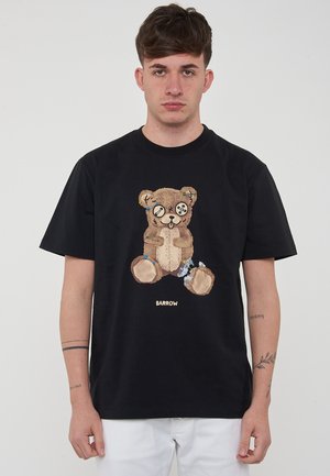 Camiseta de algodón negra con un gráfico de oso de peluche, con detalles bordados, que lleva botones como ojos y está realzada con hilos de colores.