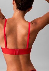 Reggiseno rosso con spalline regolabili e una fascia larga sul retro. Tessuto liscio con dettagli hardware minimi, che mette in risalto un design semplice.