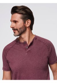Bordo tričko s krátkým rukávem henley s texturovaným povrchem, zapínání na dva knoflíky a raglánové rukávy, vystavené na modelu, který je otočený vlevo.
