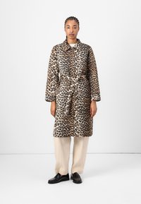 Leopardenmuster Mantel mit einem taillierten Schnitt, mittellangem Design und einem Kragen, aus einem weichen Stoff. Kombiniert mit beigen Hosen und Slippern.