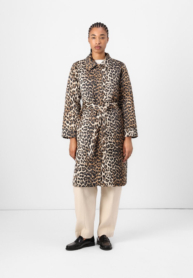 Manteau imprimé léopard avec une taille ceinturée, de coupe mi-longue et un col, fabriqué dans un tissu doux. Associé à un pantalon beige et des mocassins.