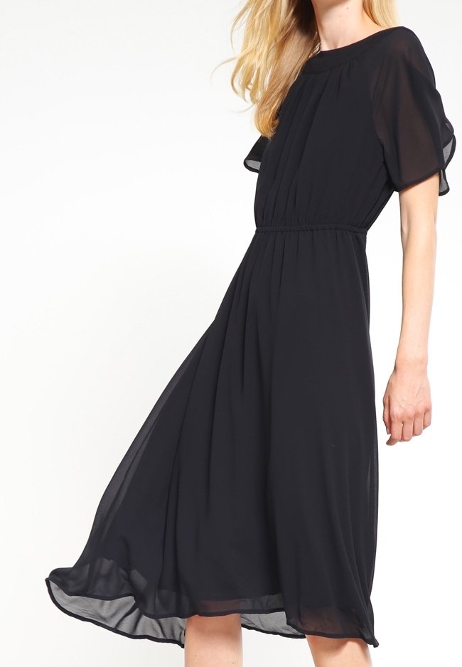 Robe en chiffon noir avec des manches courtes et flottantes, une taille élastique et une jupe midi fluide qui ondule doucement avec les mouvements.