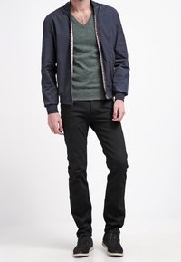 Niebieska kurtka bombowa z wzorem w kratkę wewnątrz, zielony sweter w serek, czarne dopasowane dżinsy oraz czarne buty na sznurówki z jasną podeszwą.