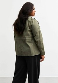 Olivegrüner, leichter Jacket mit langen Ärmeln, knöpfbarem Vorderteil und taillierter Taille. Glattes Material mit minimalistischem Design.
