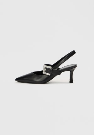Chaussure slingback en cuir noir avec bout pointu, petit talon et boucle ornée de strass. Texture lisse, design minimaliste.