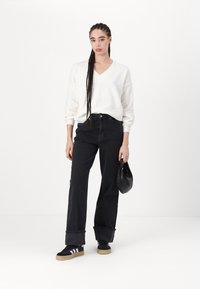 Cream V-neck sweater, high-waisted black jeans, black sneakers with white stripes, and a small black bag. Smooth fabric, relaxed fit.