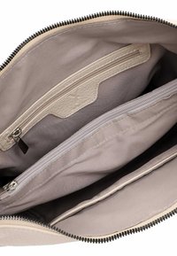 Interno di una borsa beige che mostra due scomparti con cerniera e una tasca a fessura con fodera in tessuto chiaro e rifiniture in pelle.