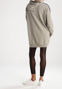 Felpa grigia oversize con cappuccio e strisce laterali, abbinata a leggings neri con un motivo a pois, completata da sneakers bianche.
