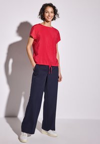 Haut court rouge à manches courtes avec un ourlet à cordon, associé à un pantalon large bleu marine et des baskets blanches. Texture lisse et coupe décontractée.