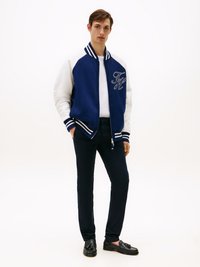 Ναυτικό μπλε varsity μπουφάν με λευκά μανίκια, ριμπ κολάρο και κεντημένα σχέδια. Συνδυάζεται με ναυτικά παντελόνια και μαύρες λοκάνες. Λείο ύφασμα.