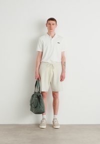 Camisa polo blanca, pantalones cortos de drapeado color beige claro, bolsa tote gris-verde, zapatos beige, fondo sencillo, diseño minimalista.