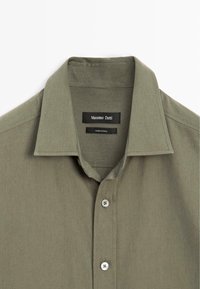 Camicia verde oliva con colletto strutturato, tessuto slim e due bottoni bianchi. Etichetta del marchio visibile all'interno del colletto.