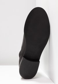 Czarny skórzany but o gładkim wykończeniu, z teksturowaną gumową podeszwą i wytłoczonym napisem "Made in Portugal". Widoczny rozmiar 37.