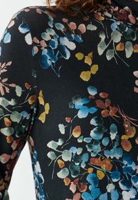 Bluse mit floralem Muster, die einen schwarzen Hintergrund und mehrfarbige Blätter in Blau, Grün, Gelb und Pink zeigt, aus weichem Stoff gefertigt.