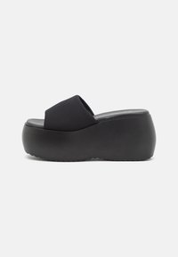 Sort platform slidesandal med tyk sål og bred stofrem over tæerne, vist fra siden på en hvid baggrund.