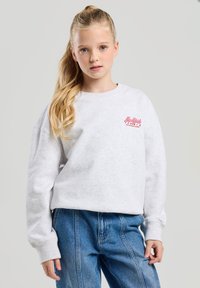 Gray, oversized sweatshirt with ribbed crew neck and cuffs. Features a pink logo on the left chest. Paired with light blue, high-waisted jeans.