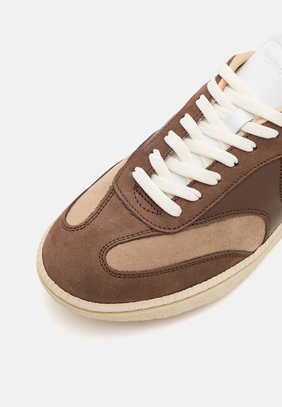 Zapatillas de ante y cuero marrón con cordones blancos, punta redonda y un panel texturizado beige. Suela de goma con borde estriado.