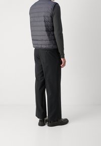 Szara, pikowana kamizelka puchowa na ciemnym swetrze; czarne spodnie o prostym kroju; czarne buty o gładkiej fakturze.