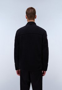 Schwarze Fleecejacke mit hohem Kragen und strukturierter Oberfläche. Sie verfügt über lange Ärmel und einen leicht lässigen Schnitt, der für Komfort sorgt.
