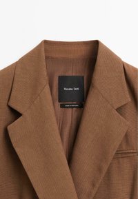 Col montant et revers de blazer marron avec une étiquette noire indiquant "Massimo Dutti" et "Fabriqué au Portugal" à l'intérieur du col.